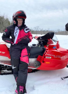 Alina Eastman outdoors, smiling on a snowmobile wearing a helmet and winter gear